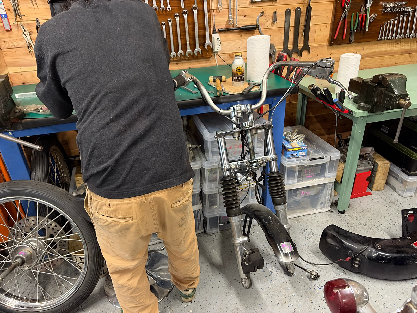 1974FXショベルヘッドから取り外したフロントフォーク、ハンドル、フェンダー、ホイールなどの部品を作業場で整理する様子